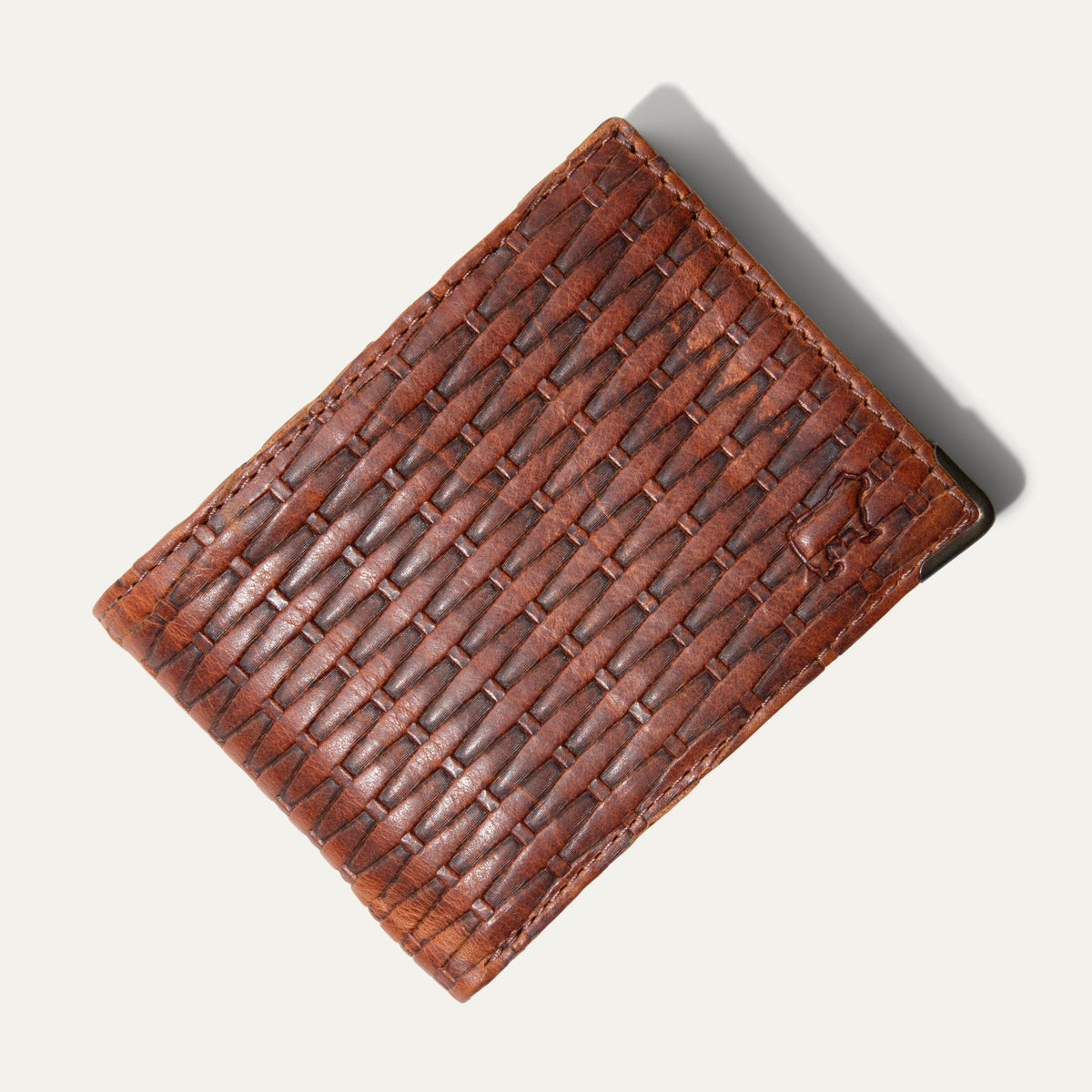 Close-up angled view of the cognac basketweave-embossed leather on the closed Mogul Billfold, showing the embossed WILL cattle logo.