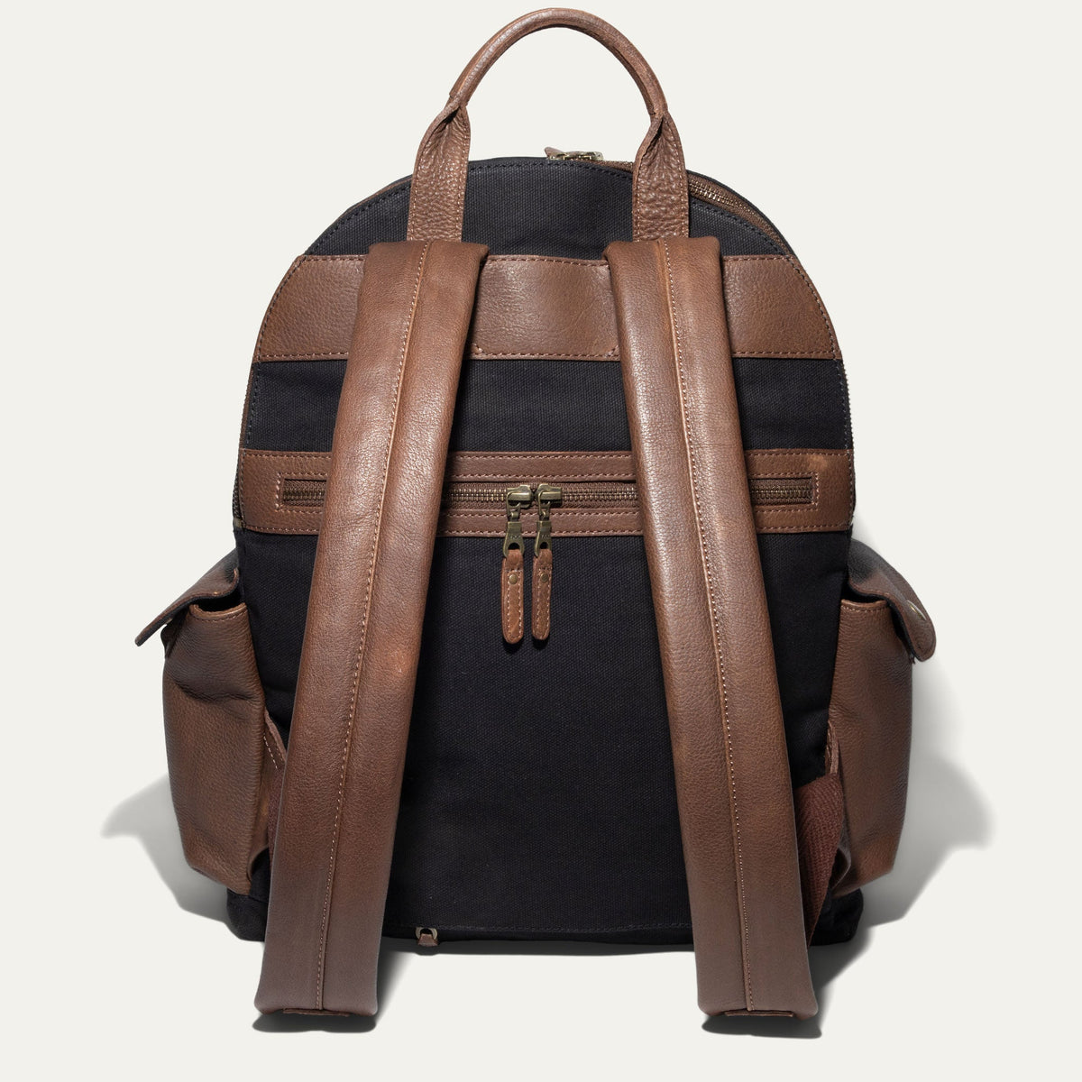 Back view of the black canvas Canvas + Leather Backpack showing the brown leather top handle, padded shoulder straps, and rear zip pocket.