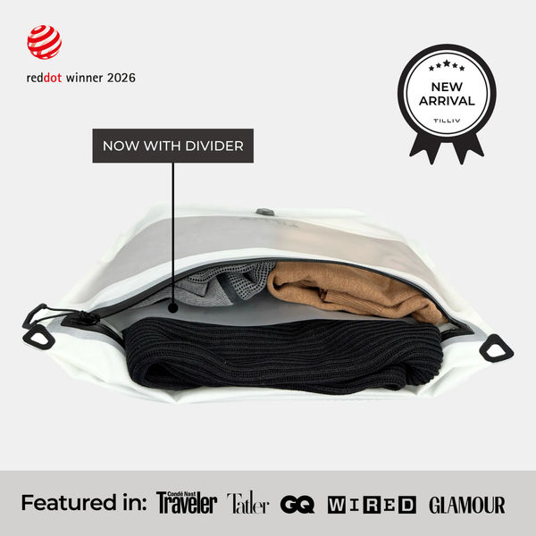 A white TILLIV Compak Medium with Divider holding black knitwear below the divider and tan and grey clothing above it, labelled Now With Divider, carrying a New Arrival badge and a strip reading Featured in Conde Nast Traveler, Tatler, GQ, WIRED and GLAMOUR