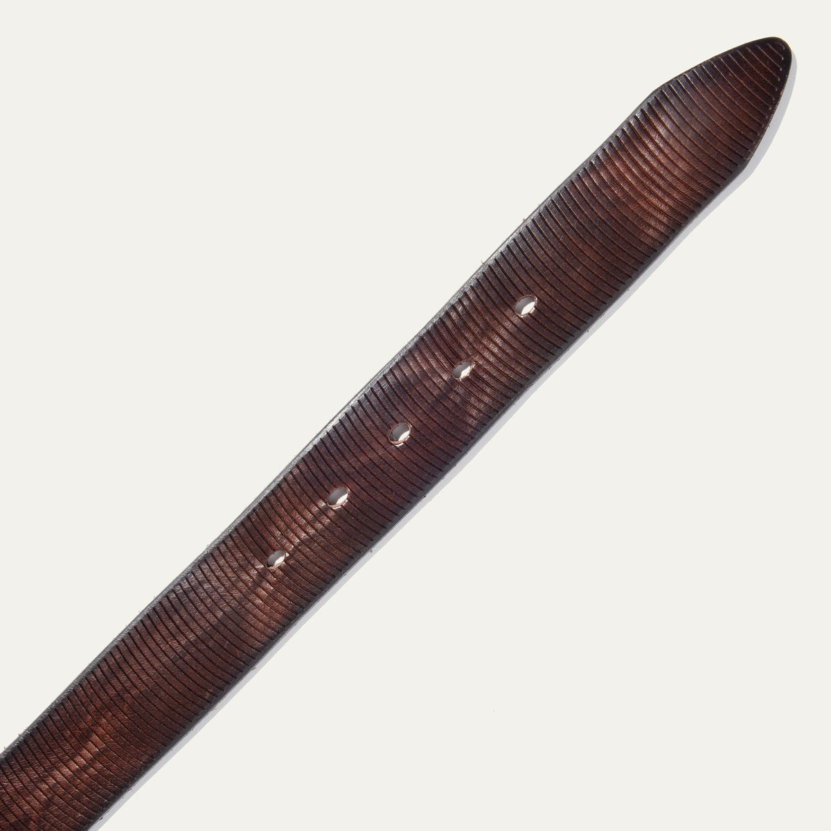 Close-up diagonal view of a warm rust-brown leather belt strap showing the fine embossed line texture and buckle holes