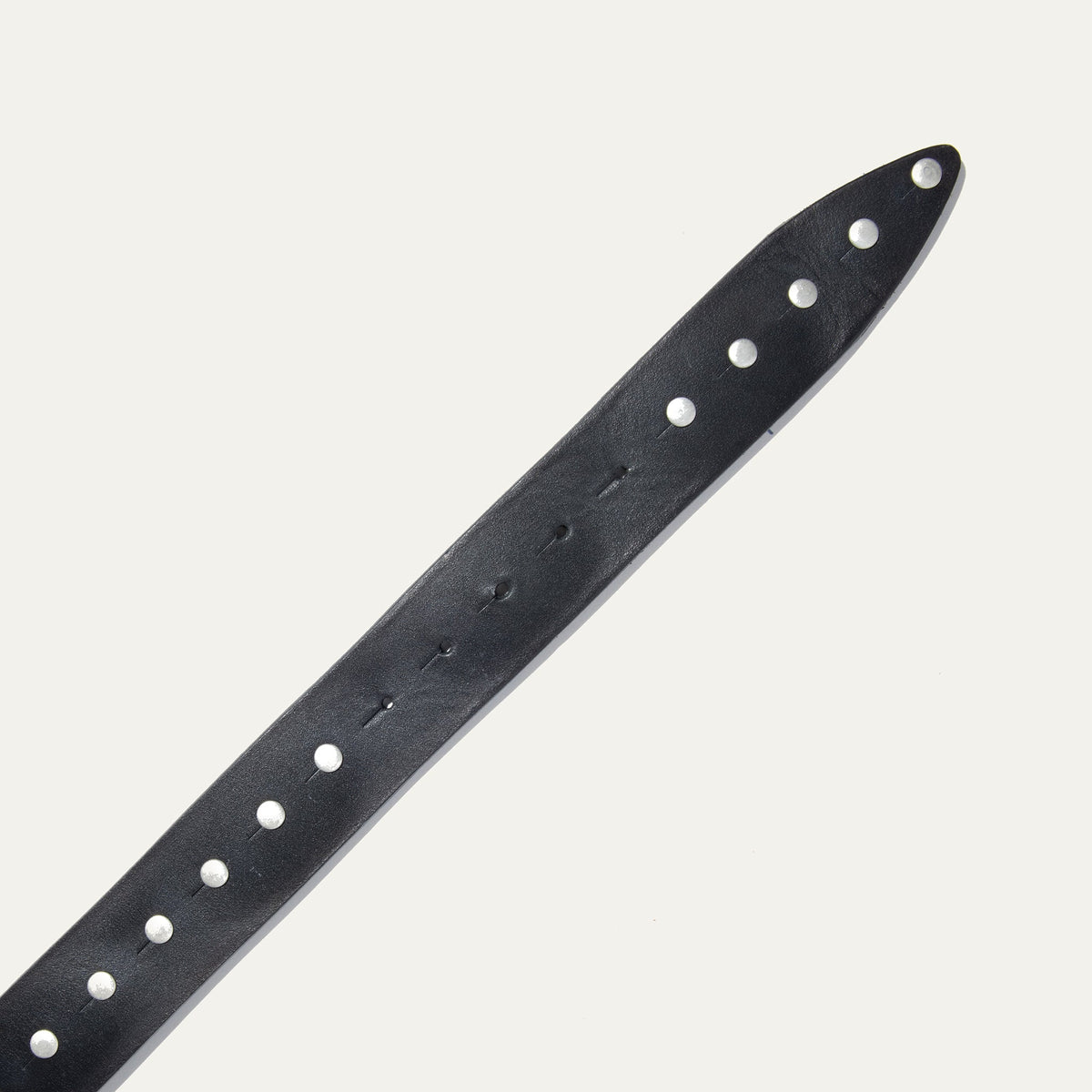 Close-up of the Will Leather Goods Single Studded Belt strap tip in black leather, showing the row of silver stud rivets and adjustment holes.