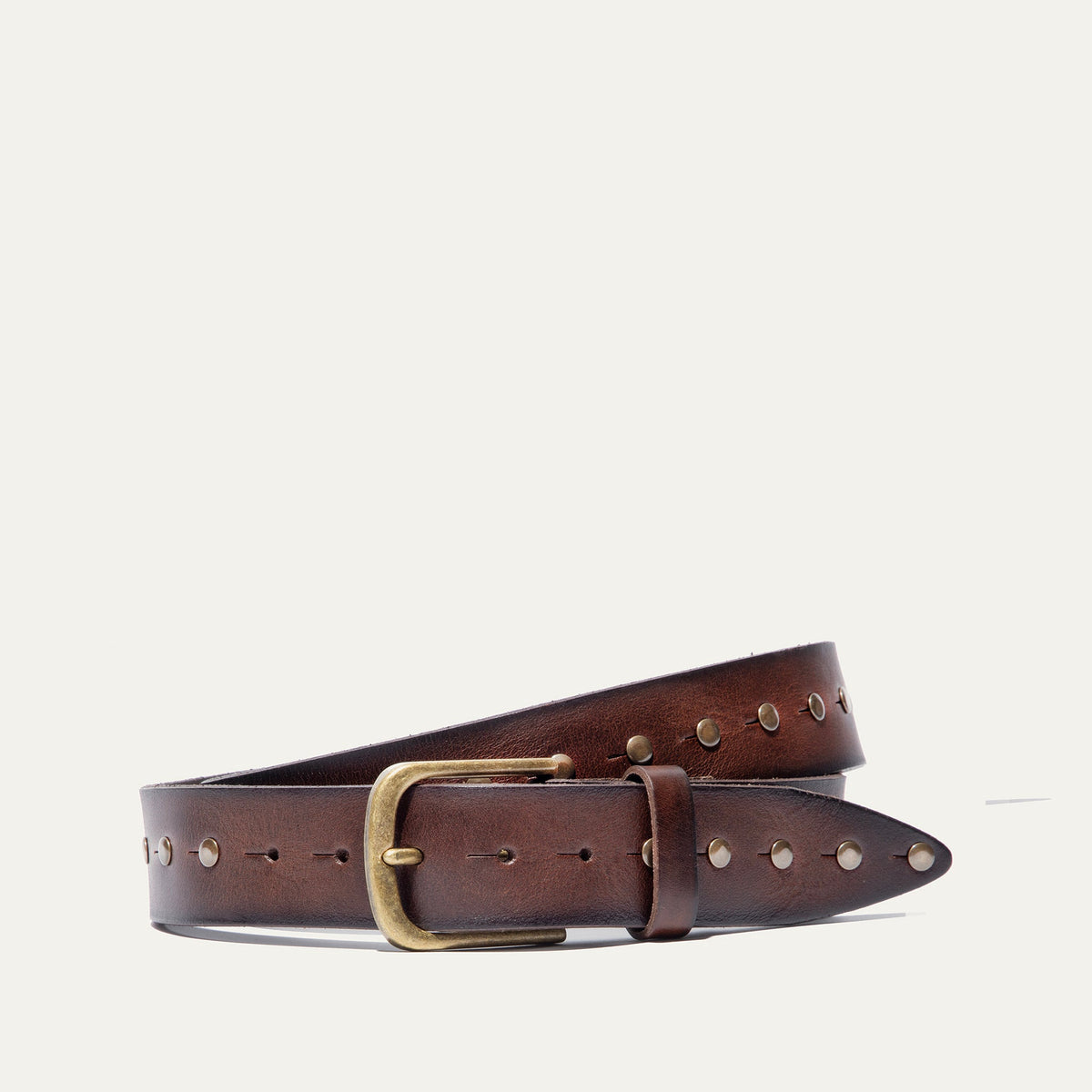Will Leather Goods Single Studded Belt in brown leather, coiled flat showing the row of antique brass stud rivets along the edge and the brass buckle, on a white background.