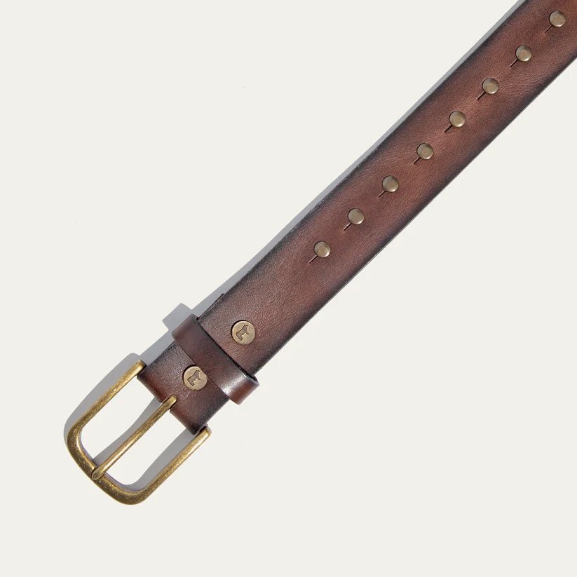 Close-up of the Will Leather Goods Single Studded Belt in brown leather, showing the antique brass buckle, keeper loop with embossed dog logo, and stud rivets.