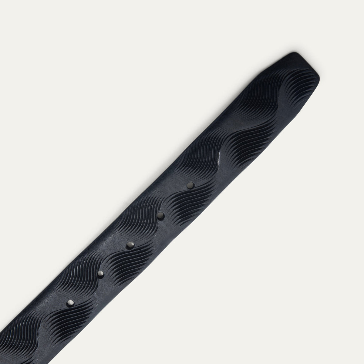 Close-up of the Will Leather Goods Wave Embossed Belt strap tip in black, showing the wave-textured embossing and adjustment holes with dark grommets.
