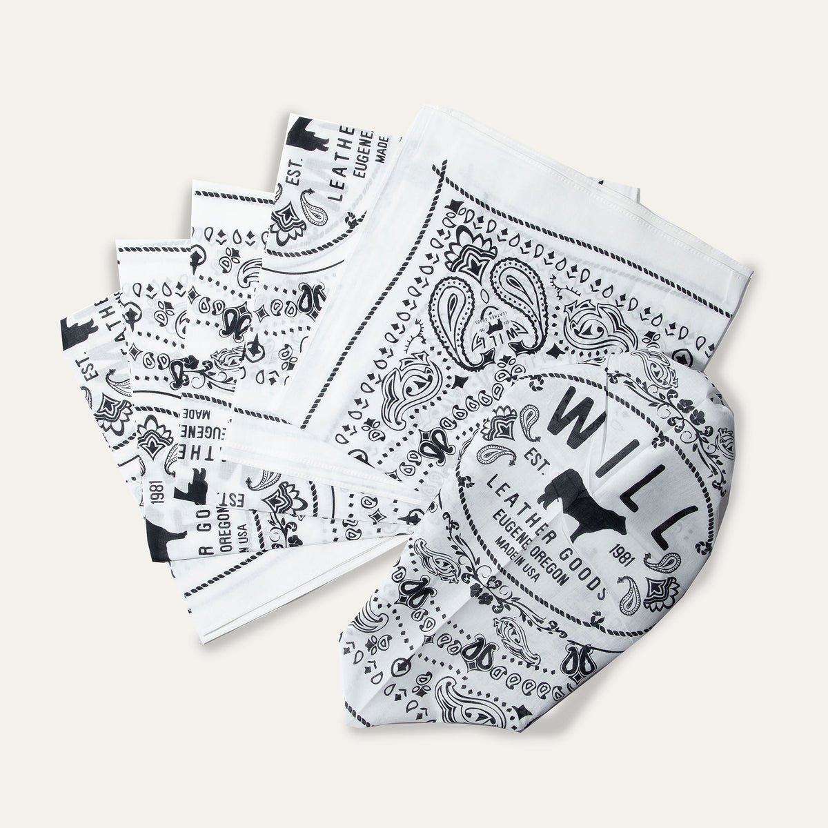Several white and black paisley Will's Bandanas fanned out to show the folded stack and logo corner detail.