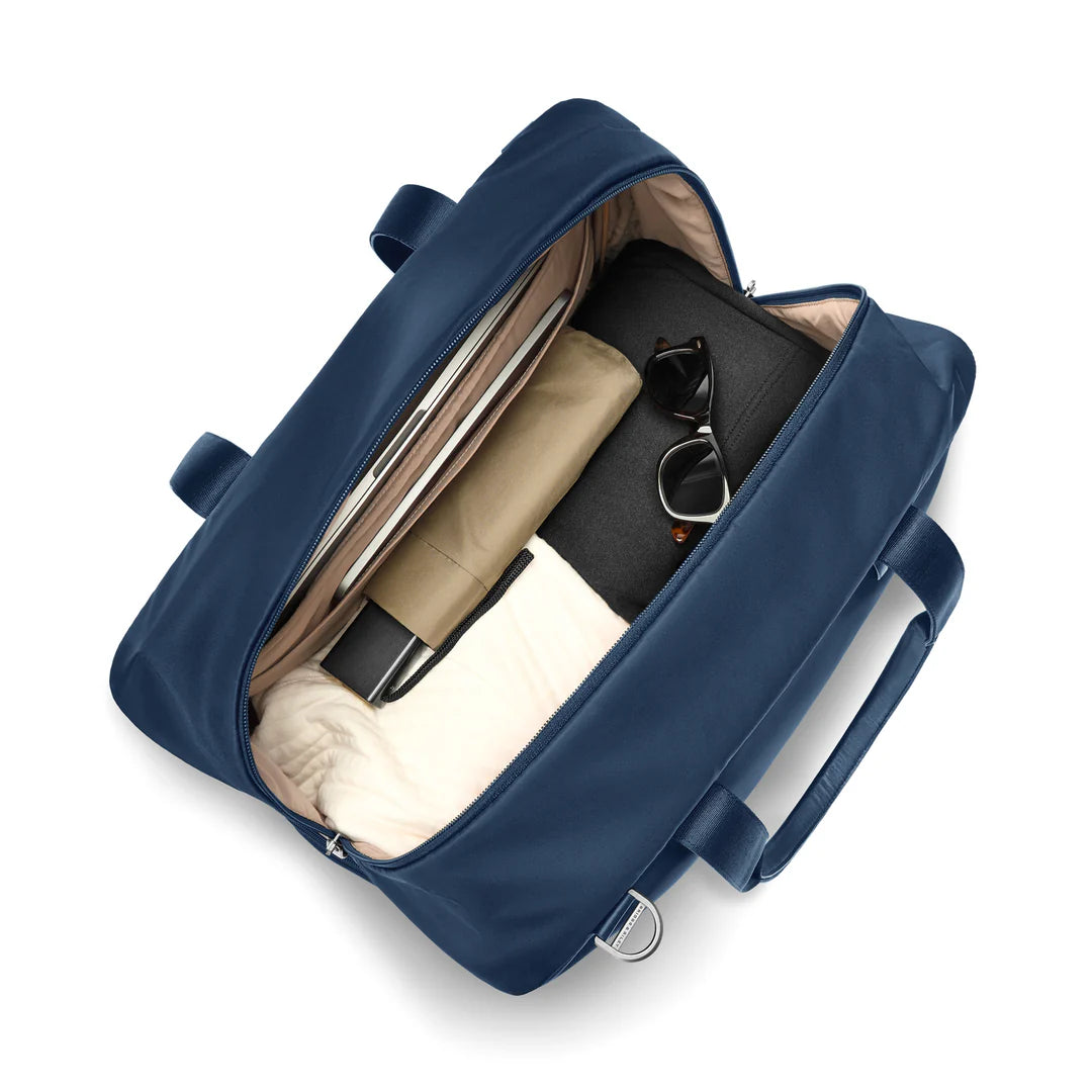 Interior of the Briggs & Riley Rhapsody Weekender Tote in navy, packed with a laptop in the padded sleeve, rolled clothing, sunglasses, and a toiletry pouch, showing the tan interior lining