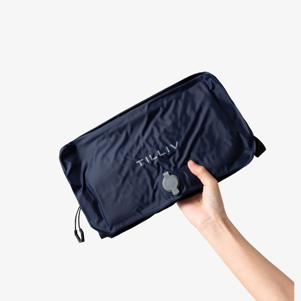A hand holding a packed Midnight Blue TILLIV Stak flat, showing its compressed depth