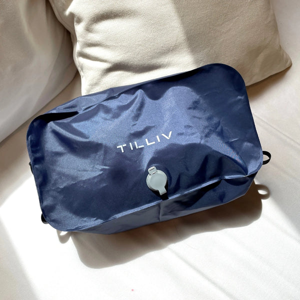 A packed Midnight Blue TILLIV Stak resting on a bed beside a cream cushion