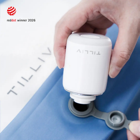 A hand holding a TILLIV Nano Pump against the open one-way valve of a Steel Blue Compak pack, with the valve cap pulled aside