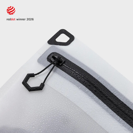 Corner of a white TILLIV Compak pack showing the hexagonal zipper pull, the triangular D-ring tab and water droplets on the fabric