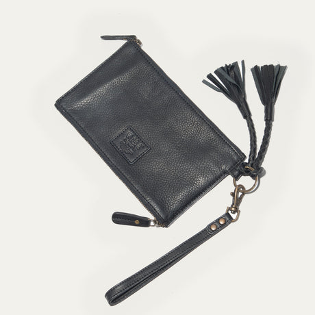 Will Leather Goods Two Zipper Pouch in black pebbled leather, closed, diagonal view on a white background, showing the embossed WILL logo patch, zipper pull, wristlet strap, and a braided leather triple-tassel keyring fob.