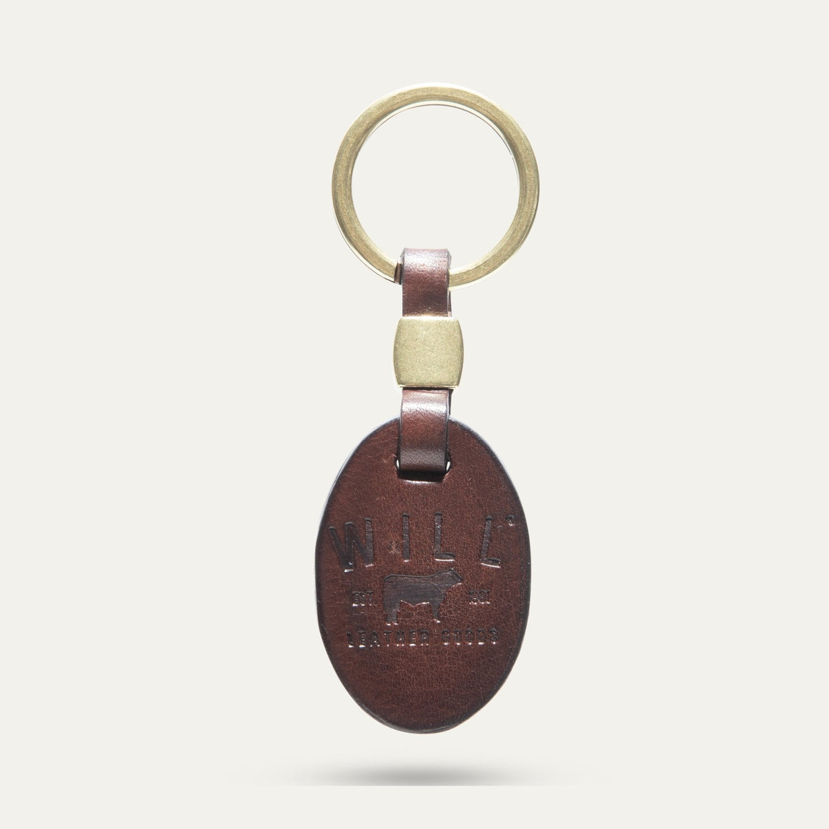 Oval leather key fob in dark brown, front view, embossed WILL Leather Goods cattle brand logo, brass key ring