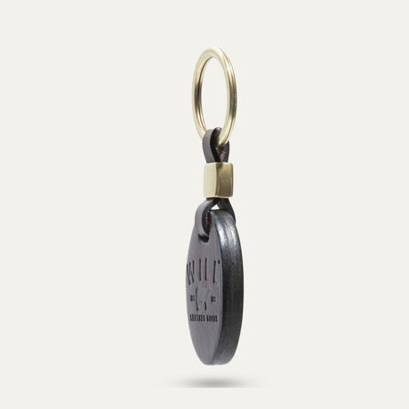 Side profile view of the dark brown leather oval key fob showing its edge and brass keyring hardware