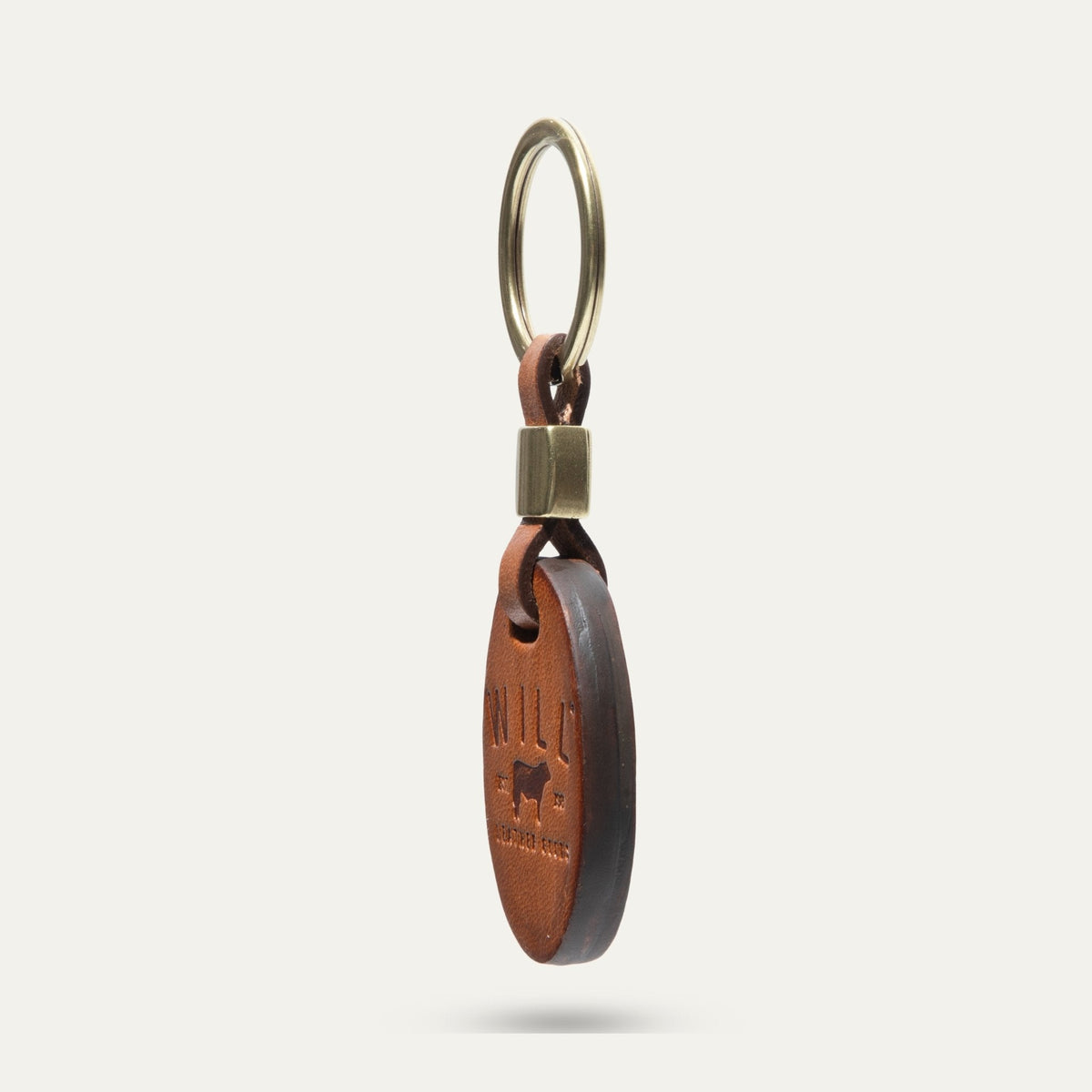Side profile view of the tan leather oval key fob showing its edge and brass keyring hardware