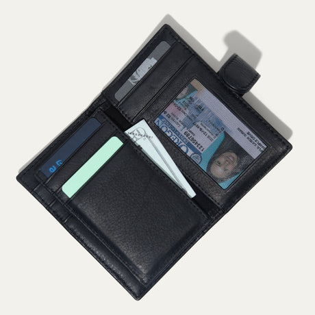 Black leather cardholder wallet open, showing card slots, a clear ID window, and a cash pocket holding a bill, on a white background.