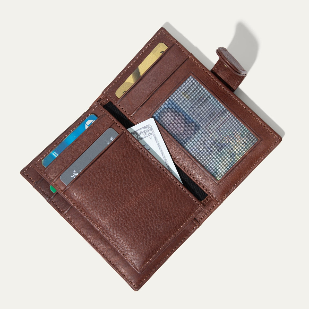 Cognac leather cardholder wallet open, showing card slots, a clear ID window, and a cash pocket holding a bill, on a white background.