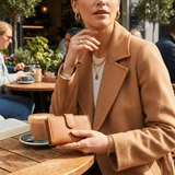 Lifestyle photo of a woman at an outdoor cafe table holding the tan leather cardholder wallet next to a latte and an open book.