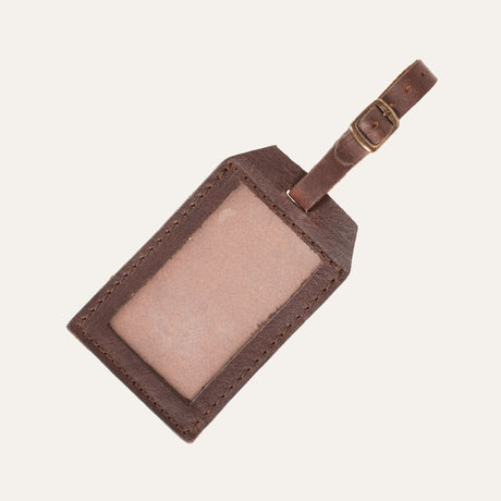 Dark brown leather luggage tag showing the clear ID window insert side, with the buckled leather loop strap