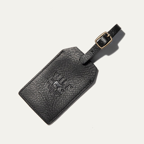 Black leather luggage tag shown at an angle, with the embossed WILL Leather Goods logo and a buckled leather loop strap