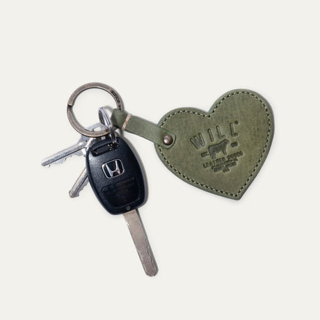 Will Leather Goods Heart Keychain in sage green leather with embossed WILL logo, attached by a brass ring to a Honda car key and two household keys, on a white background.