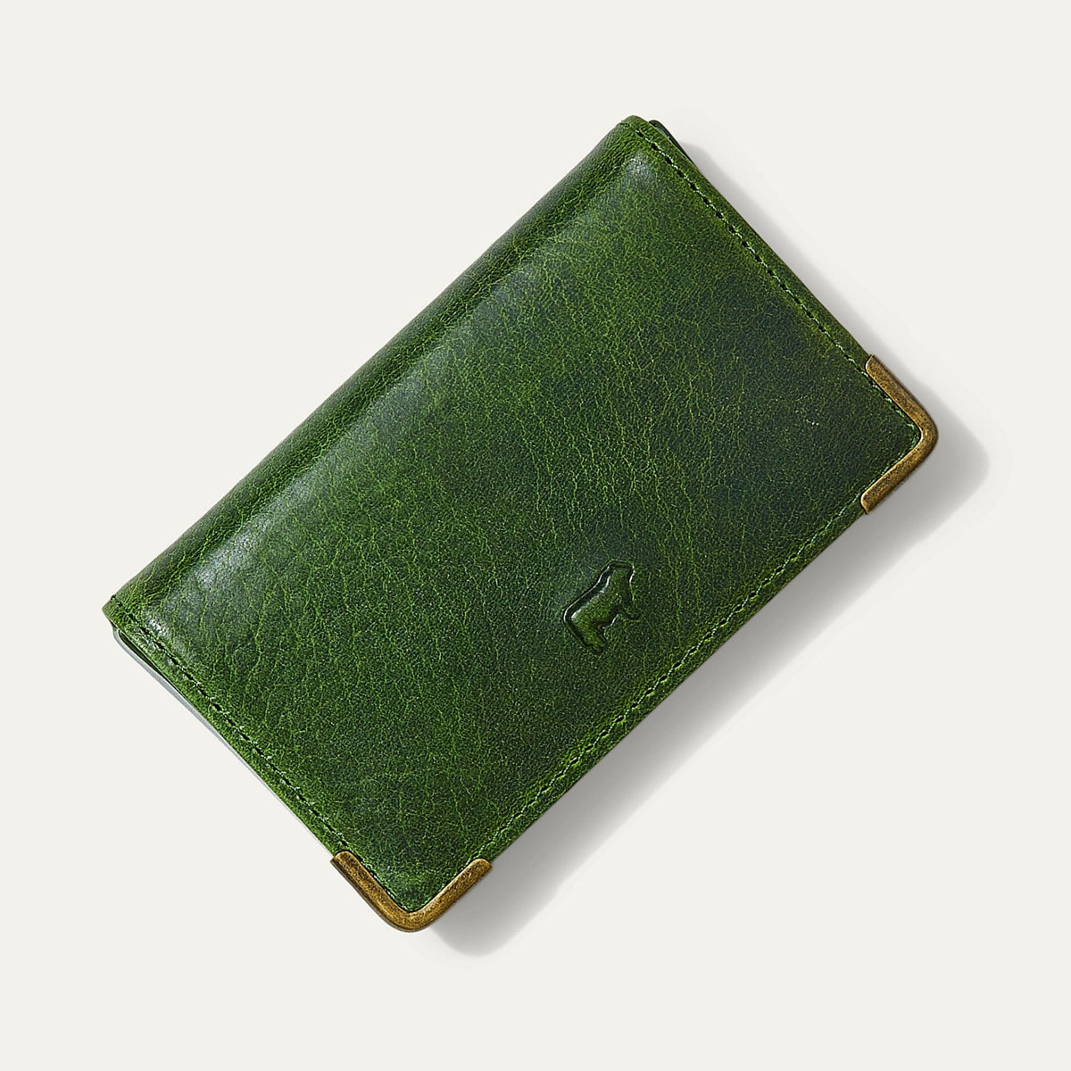 Will Leather Goods green leather trifold business card holder, corner angle view showing brass corner guards and embossed cattle logo