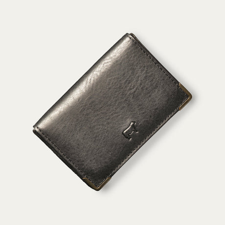 Will Leather Goods black leather trifold business card holder, corner angle view showing brass corner guards and embossed cattle logo