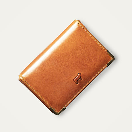 Will Leather Goods cognac leather trifold business card holder, corner angle view showing brass corner guards and embossed cattle logo