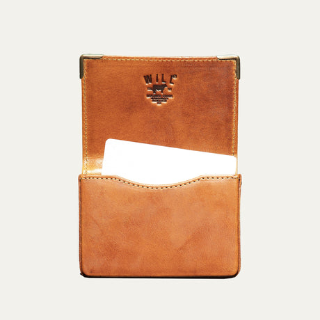 Close-up of the cognac leather card holder's brass corner guard and edge stitching
