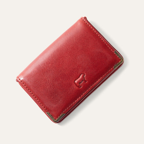 Will Leather Goods red leather trifold business card holder, corner angle view showing brass corner guards and embossed cattle logo