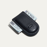 Will Leather Goods Classic Money Clip in black leather holding folded cash, top-down view with embossed cattle logo, on a white background.