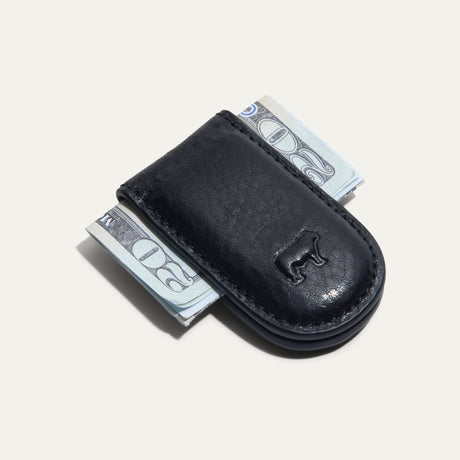 Will Leather Goods Classic Money Clip in black leather holding folded cash, top-down view with embossed cattle logo, on a white background.