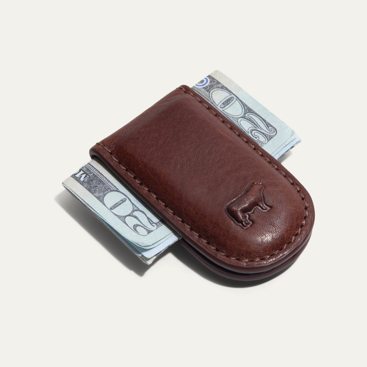 Will Leather Goods Classic Money Clip in cognac leather holding folded cash, top-down view with embossed cattle logo, on a white background.