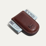 Will Leather Goods Classic Money Clip in cognac leather holding folded cash, top-down view with embossed cattle logo, on a white background.