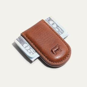 Will Leather Goods Classic Money Clip in tan leather holding folded cash, top-down view with embossed cattle logo, on a white background.