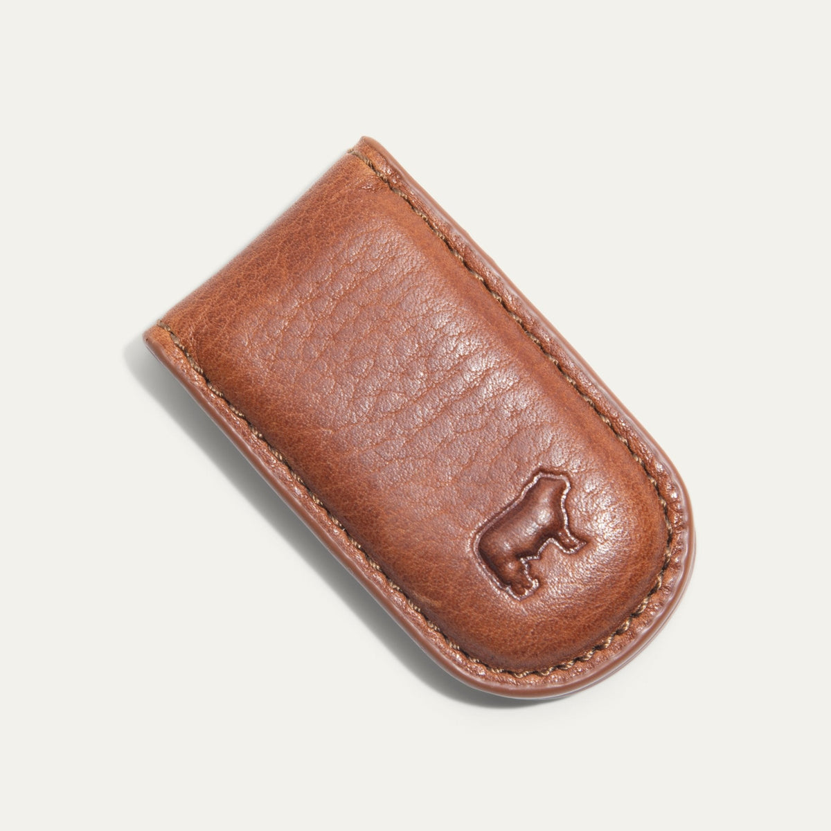 Angled close-up of the tan Classic Money Clip holding cash, showing the stitched edge and embossed WILL cattle logo.