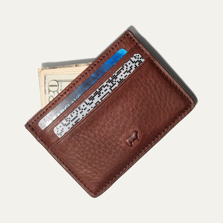 Cognac leather card case holding several cards and folded cash fanned out from the front pocket, on a white background.