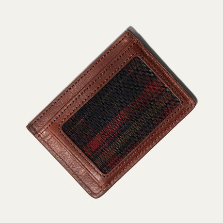 Cognac leather card case flat lay showing the clear ID window backed with black, red, and tan plaid fabric, on a white background.