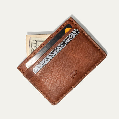 Tan leather card case holding several cards and folded cash fanned out from the front pocket, on a white background.