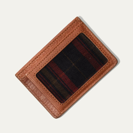 Tan leather card case flat lay showing the clear ID window backed with black, red, and tan plaid fabric, on a white background.