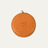 Cognac tan round leather tape measure case with embossed cow logo, front view showing a metal loop attachment at the top.