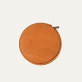 Cognac tan round leather tape measure case, angled view showing smooth leather texture and the metal loop attachment at the top.