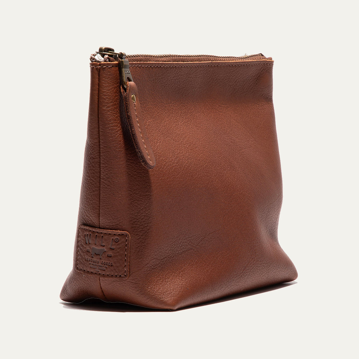 Cognac leather zip pouch shown from a three-quarter angle, highlighting the trapezoid shape and zipper pull