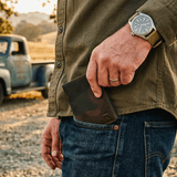 Lifestyle photo of a man's hand pulling the green camo Military Front Pocket wallet from his jeans back pocket, vintage pickup truck in the background.