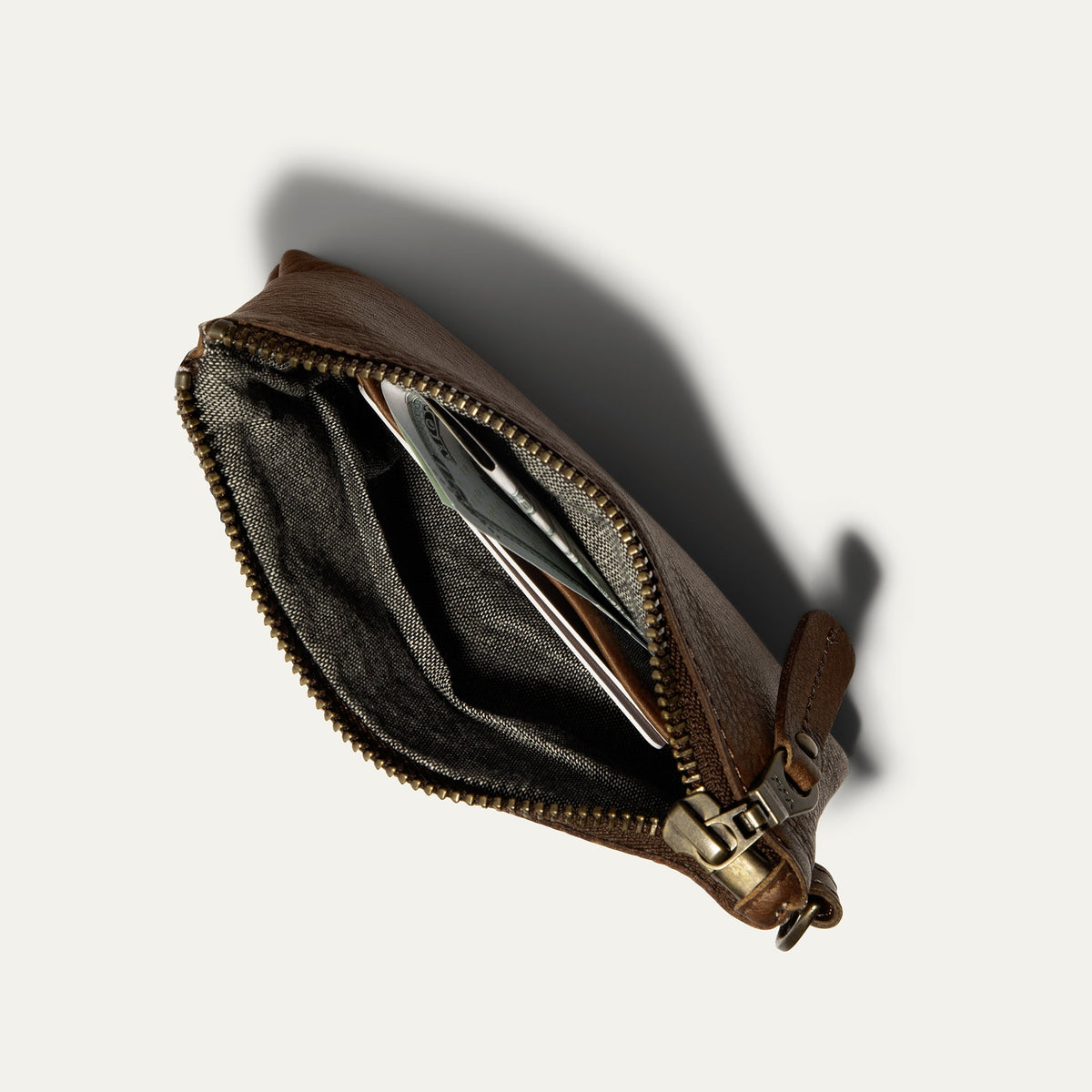 Cognac leather zip pouch unzipped, showing interior card slots and cash tucked inside