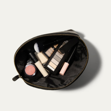 Overhead view of the black Zip Cosmetic bag open, unzipped to show the black mesh interior filled with makeup brush, eyeshadow palette, concealer, and blush.