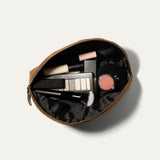 Overhead view of the tan Zip Cosmetic bag open, unzipped to show the black mesh interior filled with concealer, eyeshadow palette, lip balm, and a makeup brush.