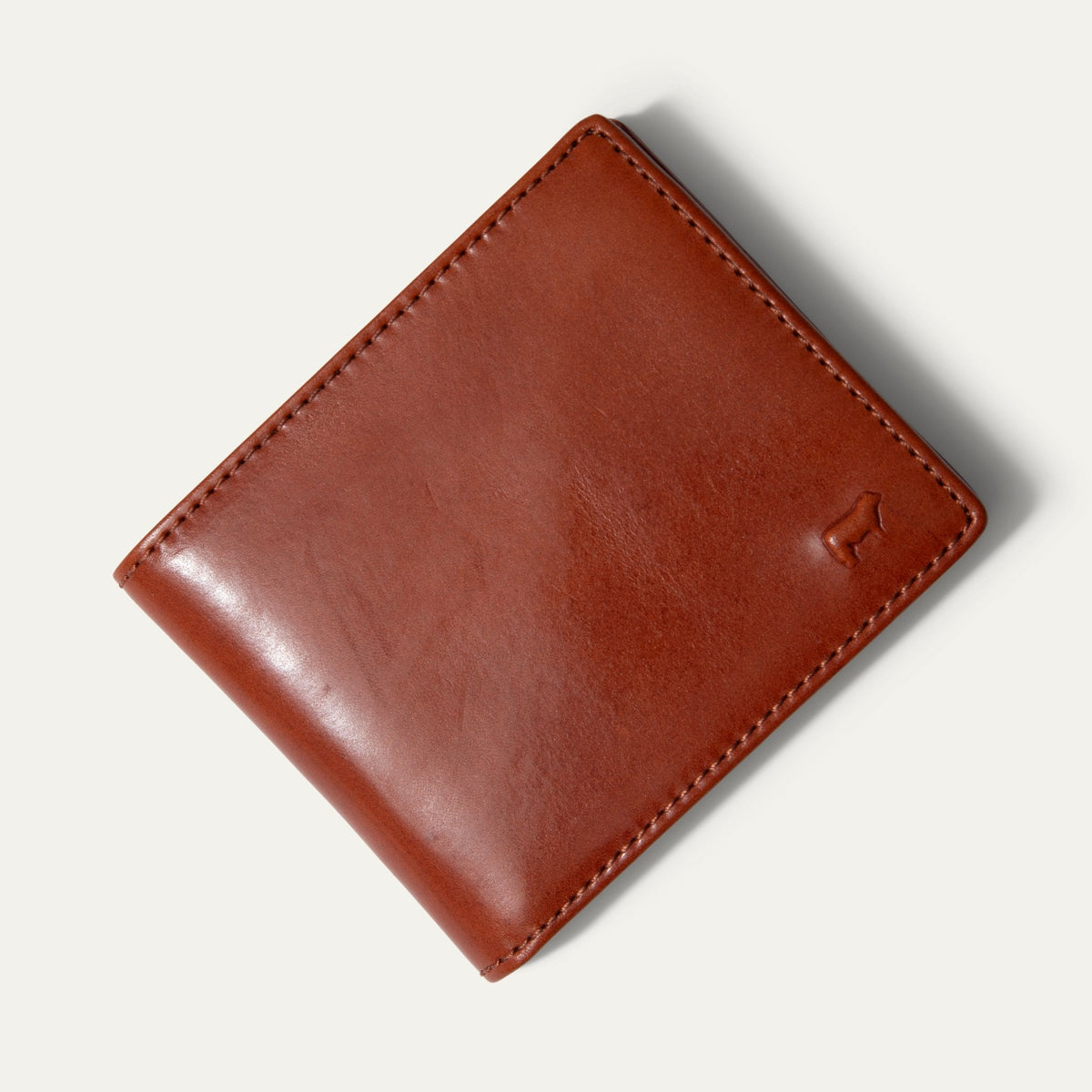 Will Leather Goods Classic Billfold Wallet in amber/cognac leather, closed, angled front view showing the embossed cattle-brand logo, on a white background.