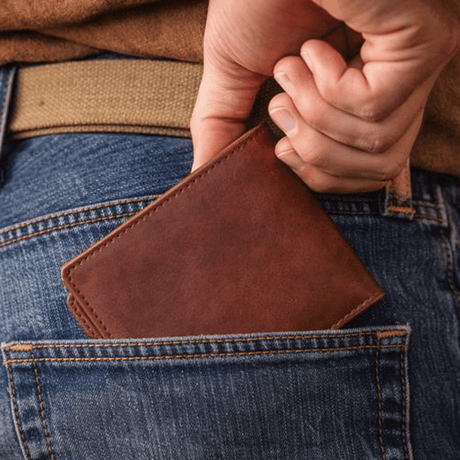 Lifestyle photo of a cognac leather billfold wallet being tucked into the back pocket of blue jeans.
