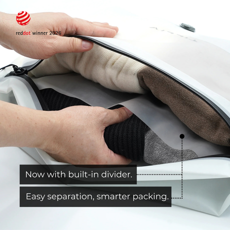 Hands lifting the grey divider inside a white Compak Large to separate black knitwear from cream and brown clothing, captioned Now with built-in divider, easy separation, smarter packing