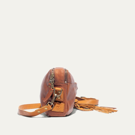 Side view of the cognac and tan leather crossbody bag showing the adjustable strap, zipper pulls, and fringe tassel